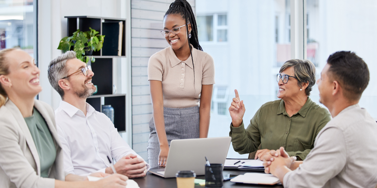 five people talking in an office, sitting and standing around a table