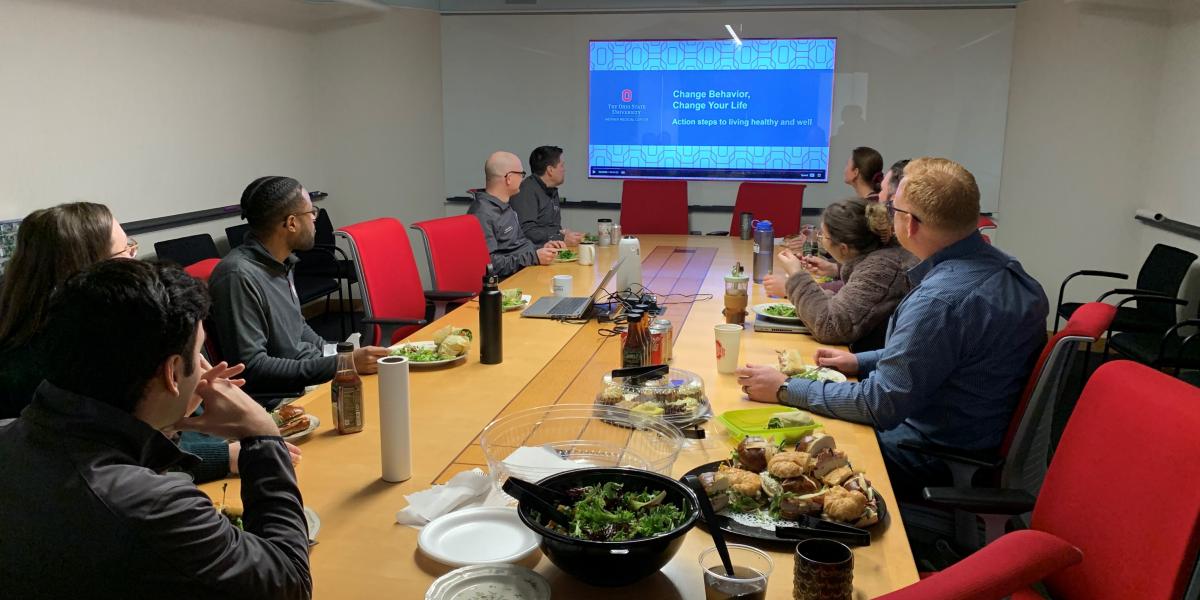 group in conference room looking at screen eating balanced lunch