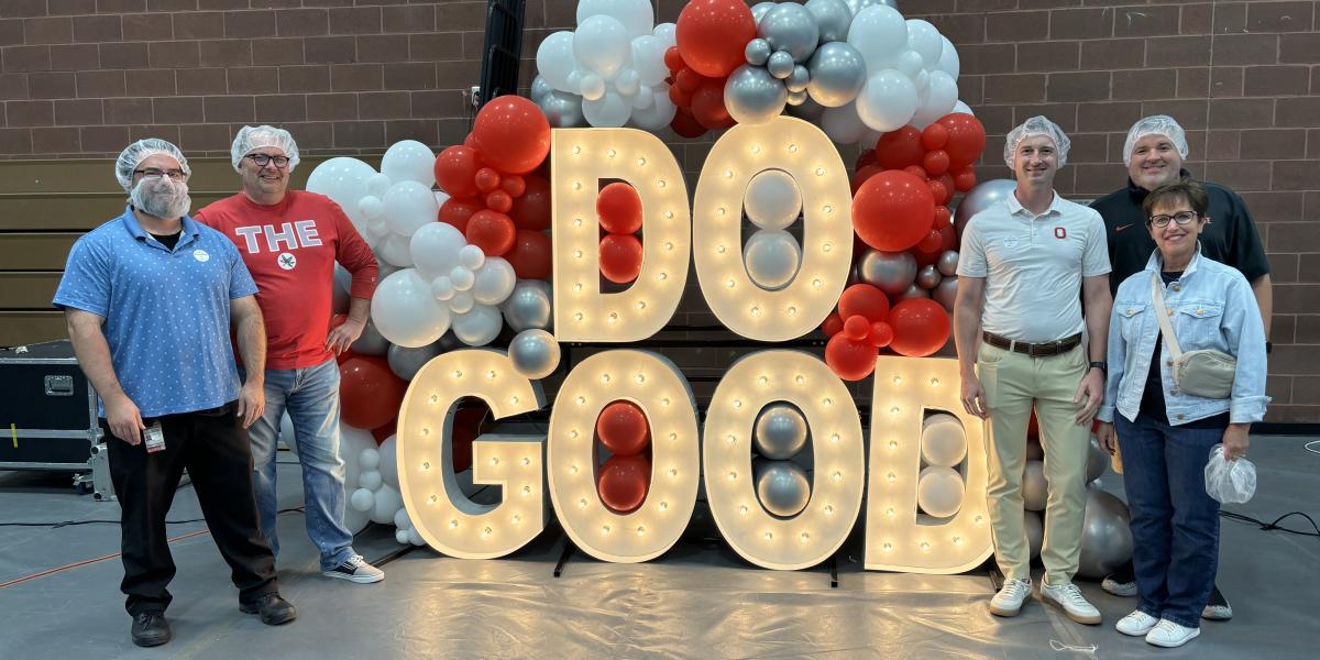 Five people standing on each side of large, lit up letters that spell out, 'DO GOOD'