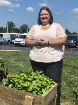 A photo of Christina Miller standing behind the raised garden bed smiling while holding freshly picked jalapeños.