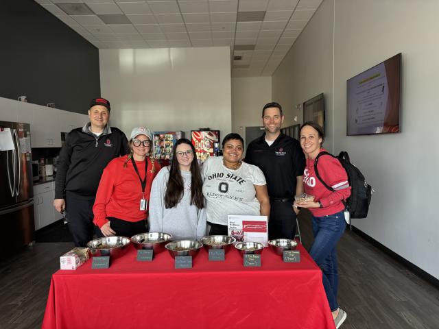 Six people stand behind a table with trail mix ingredients smiling for a photo.